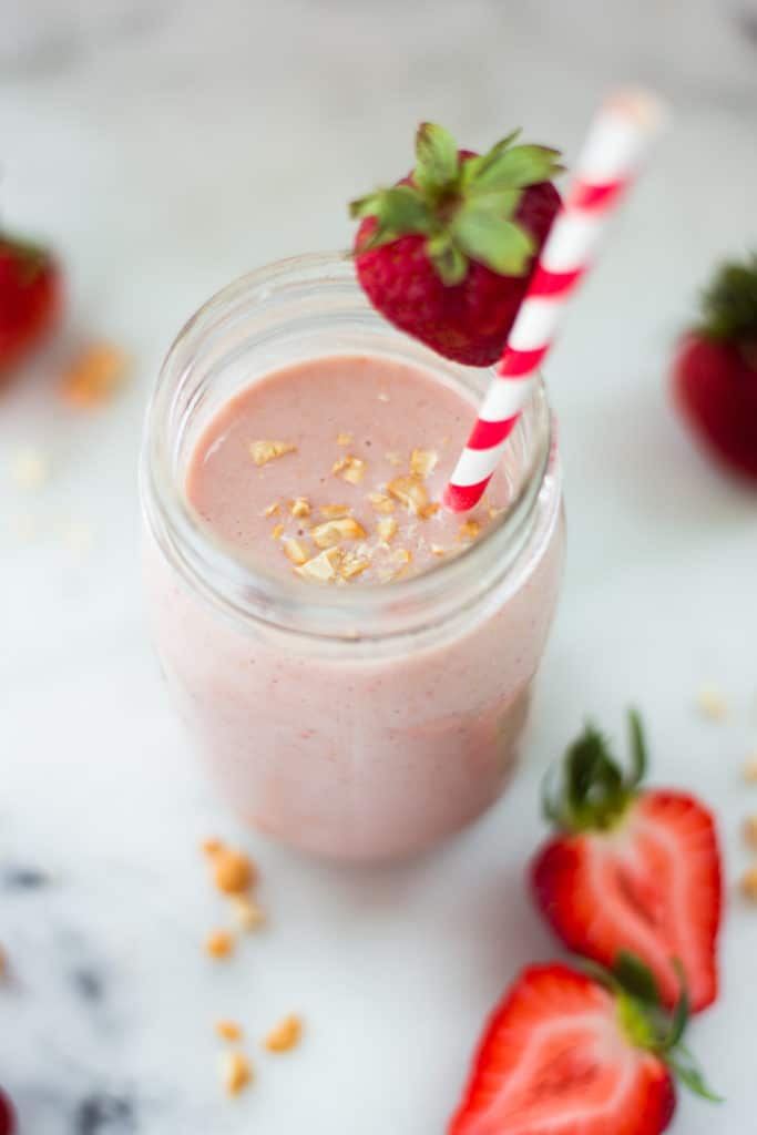 Overhead image of a mason jar filled with a strawberry protein smoothie, with sliced strawberries around the jar.