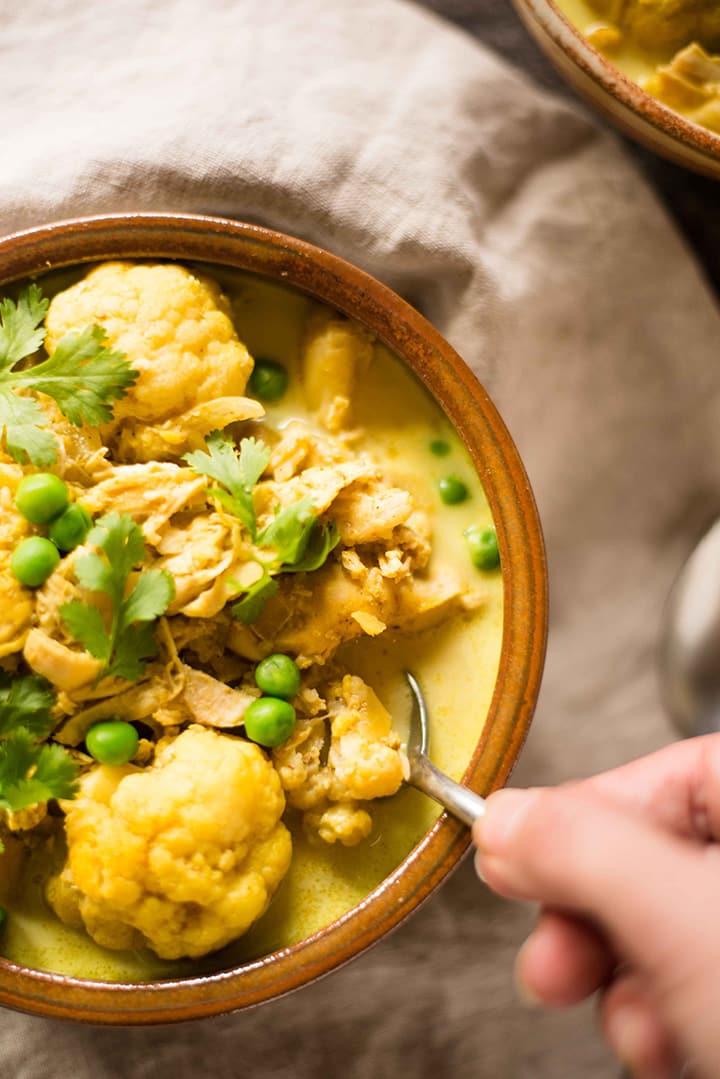 Overhead image of a hand with spoon scooping out some of the slow cooker chicken cauliflower curry from the bowl.