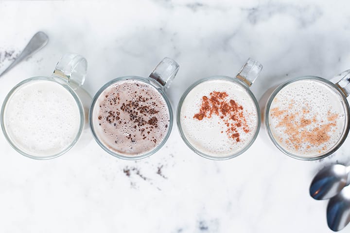 Top view of the 4 homemade lattes including eggnog latte, chai latte, vanilla latte, and mocha latte in mugs, garnishes and ready to be served.