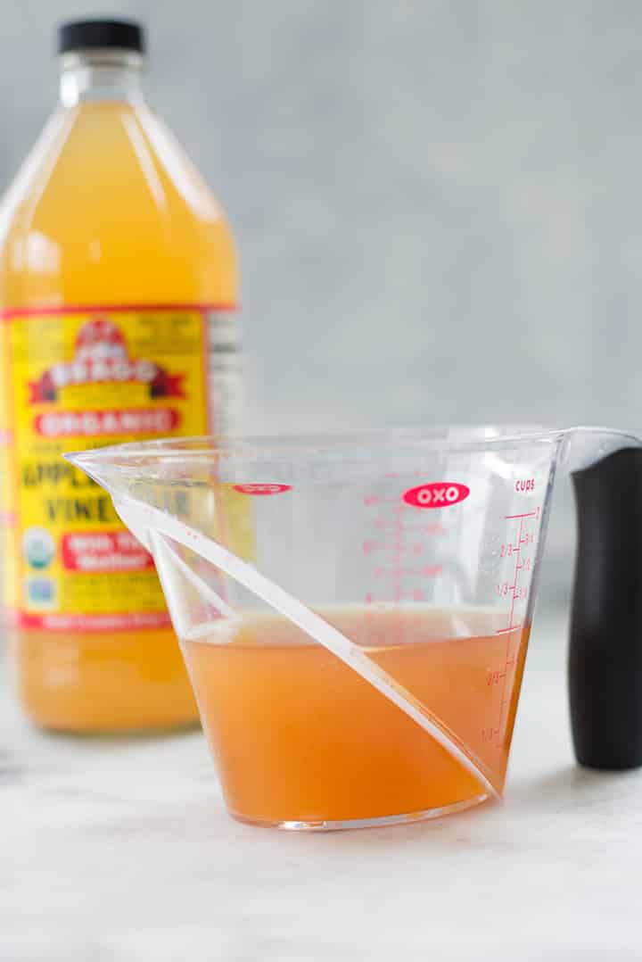 Apple cider vinegar in a measuring cup. In the background can be seen the bottle of organic apple cider vinegar.