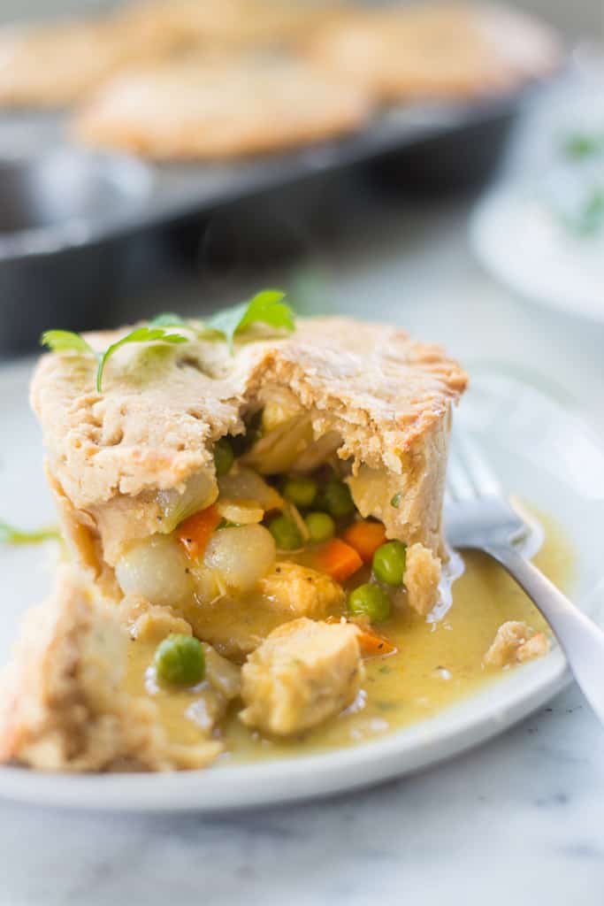 Side view image of a chicken pot pie portion on a white plate, with chicken, topping, carrots, and peas.