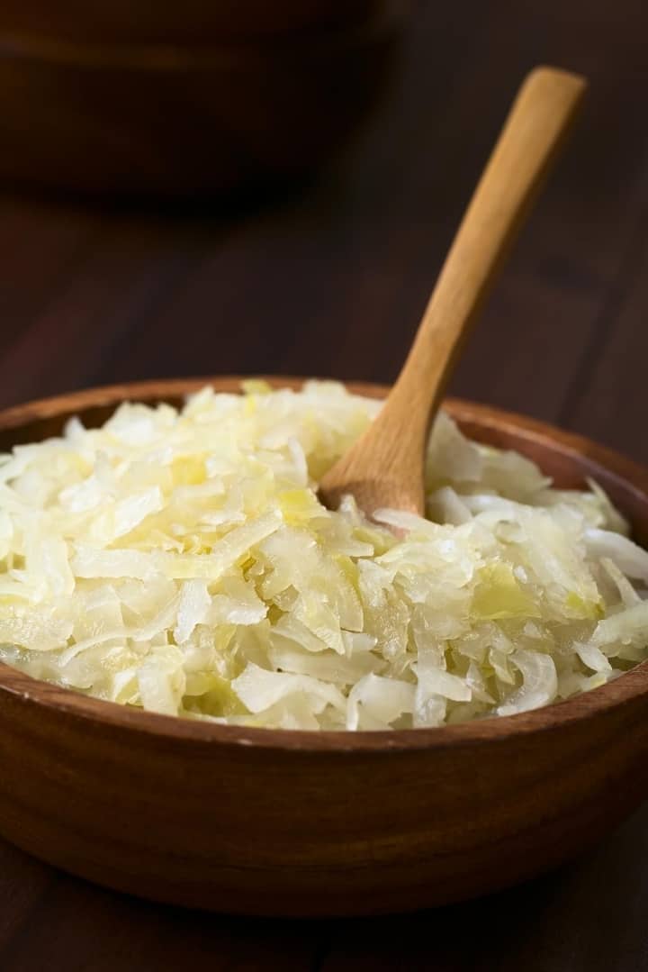 Close up view of a wooden bowl filled with sauerkraut, with a wooden spoon in the bowl.