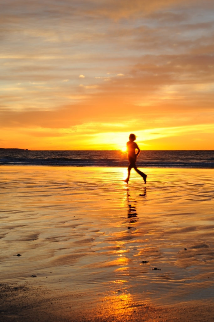 Image of a person running on the beach with the tide out at sunset.