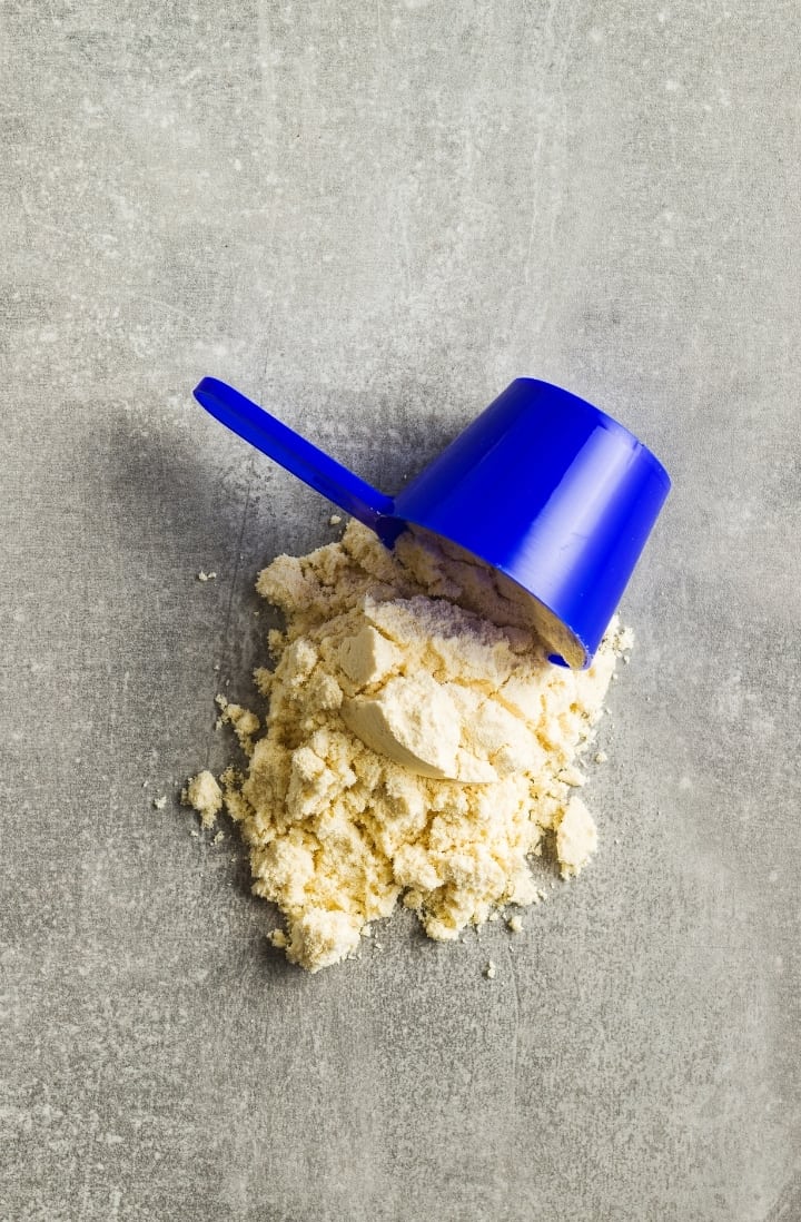 Close up view of a blue scoop on its side, with pea protein powder poured on a surface.