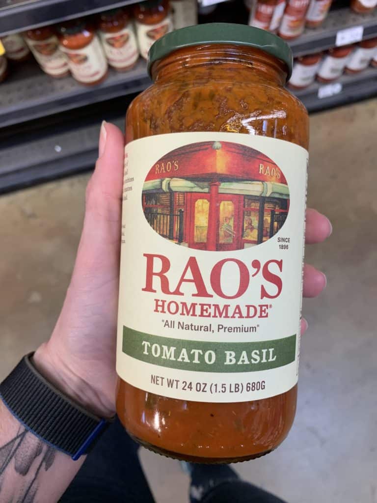 Close up image of a hand holding a large jar of Rao's pasta sauce.