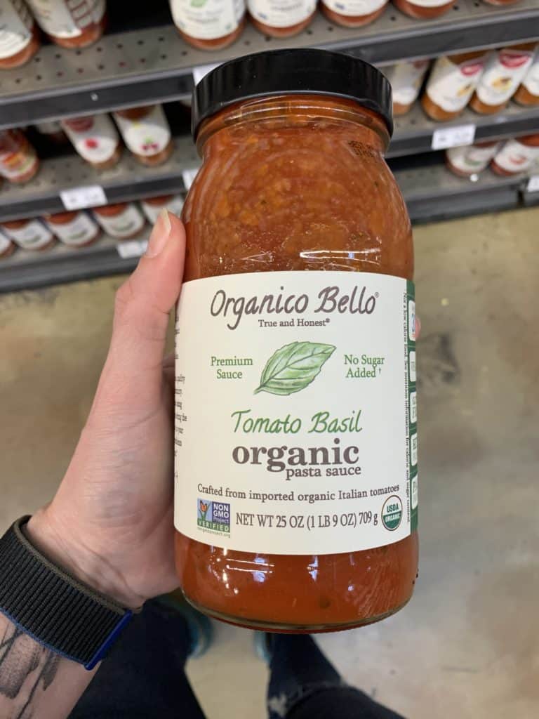 Close up image of a hand holding a large jar of Organico Bello pasta sauce.