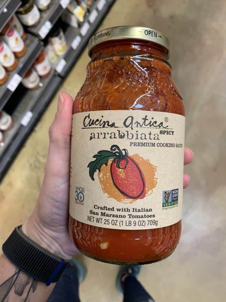 Close up image of a hand holding a large jar of Cucina Antica pasta sauce.
