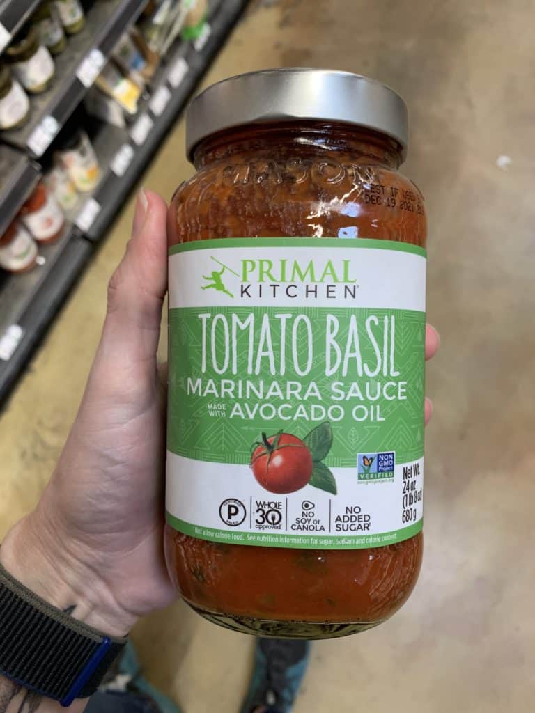Close up image of a hand holding a large jar of Primal Kitchen pasta sauce.