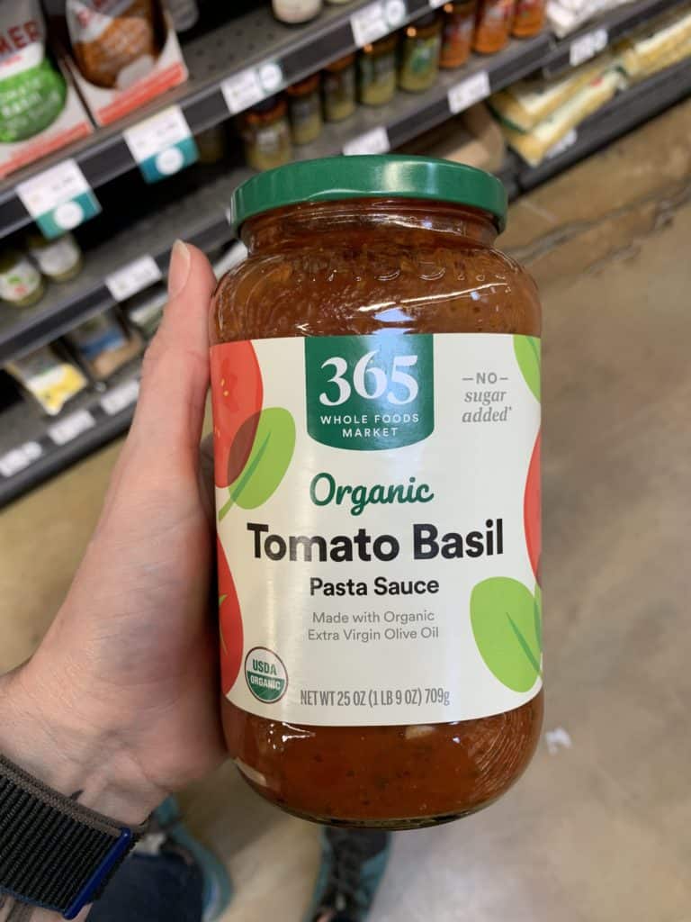 Close up image of a hand holding a large jar of 365 Whole Foods Market pasta sauce.
